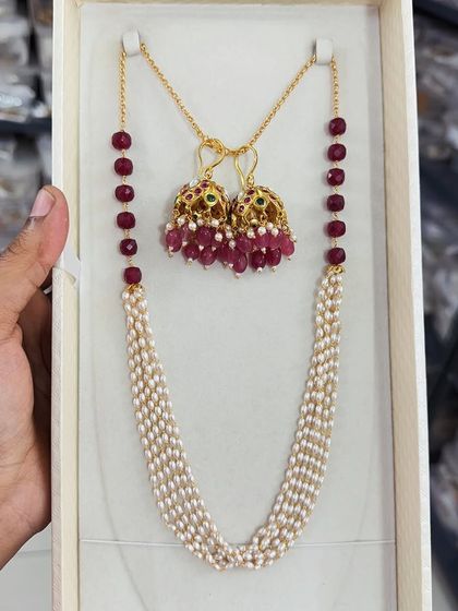 This premium beaded jewelry set combines a multi-strand pearl necklace with beautiful ruby-beaded jhumki earrings. It's a classic and elegant combination perfect for traditional wear.