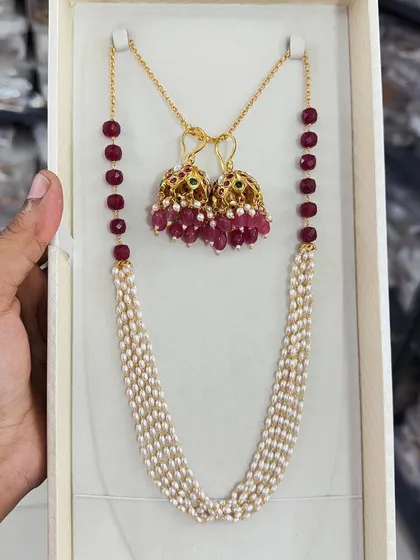This premium beaded jewelry set combines a multi-strand pearl necklace with beautiful ruby-beaded jhumki earrings. It's a classic and elegant combination perfect for traditional wear.
