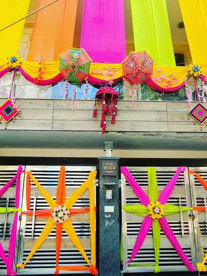 A decorated gate with colourful star-shaped fabric designs, matching the vibrant drapes on the house front.