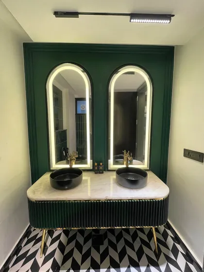 A finished powder room featuring a custom fluted vanity in green, a marble countertop with dual vessel sinks, and bold black-and-white geometric flooring.