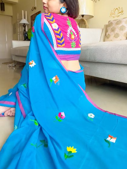 A seated pose showing how the blouse looks from the side. The vibrant colors stand out beautifully against the blue of the saree.
