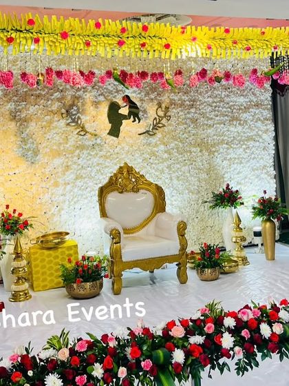 A beautiful Seemantham stage with a backdrop made entirely of fresh white flowers. The design is personalized with a mother and child silhouette and accented with red and pink floral arrangements.