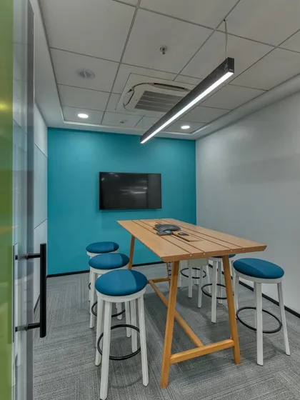 A huddle room with a high table and stools, encouraging shorter, more active meetings. The teal accent wall adds a pop of color.
