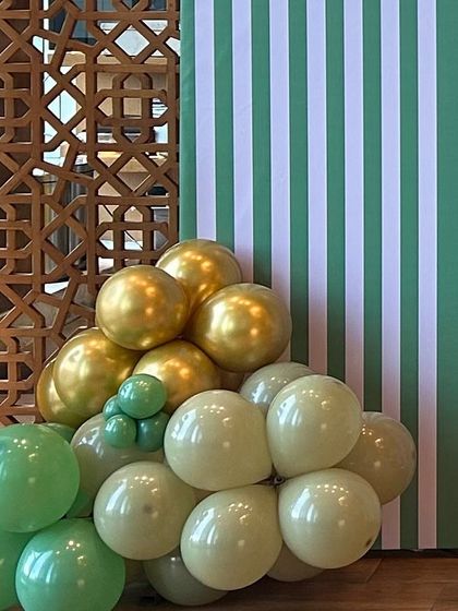A detail shot of a modern safari-themed setup. The green and white striped backdrop is paired with a simple balloon cluster in muted green and gold tones.