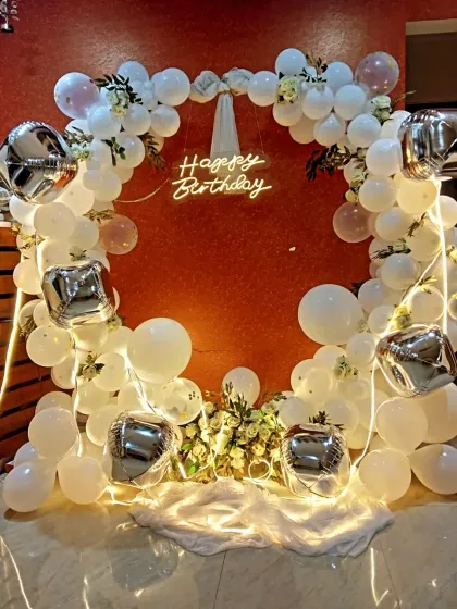 A heart-shaped balloon arch in white and silver, with a "Happy Birthday" neon sign. This is a perfect photo booth for a birthday celebration.