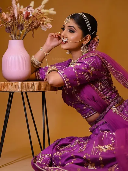 An elegant studio portrait of a model in a purple lehenga, posing with a modern vase.
