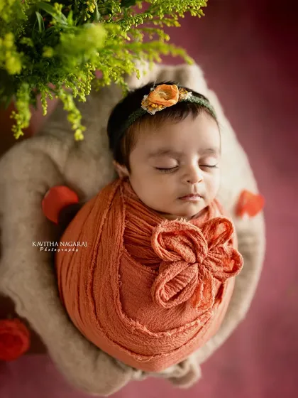 Wrapped in a warm, rust-colored swaddle with a matching floral headband, this baby’s gentle smile is like a soft melody. A perfect portrait of peaceful sleep.