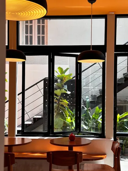 Inside DRIP & DROP, showing how natural light fills the space through large windows. The design combines modern pendant lighting and warm wood furniture to create a comfortable, energetic atmosphere for a specialty coffee shop.
