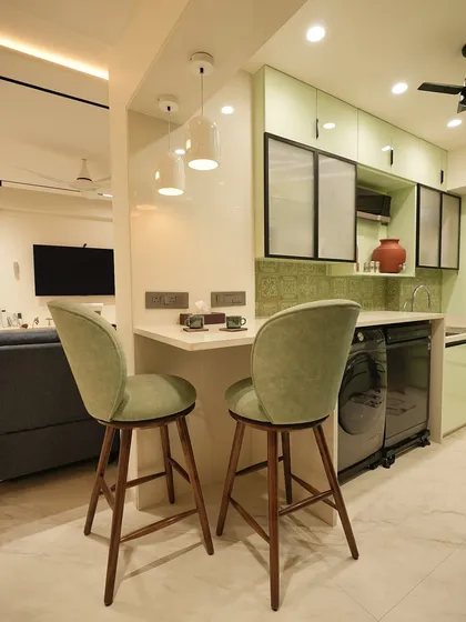 A close-up of the breakfast counter that separates the kitchen from the living area. The sage green chairs and simple pendant lights create a charming spot for morning coffee or casual meals.