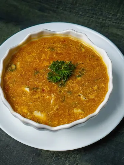 A bowl of creamy sweet corn soup, presented simply in a white bowl on a dark surface. The moody lighting adds depth and texture to the shot.