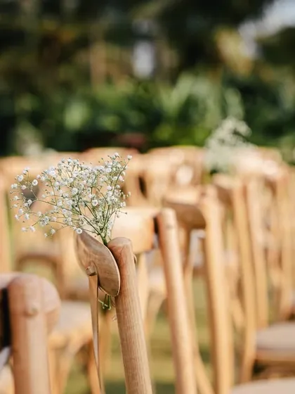 Minimalist decor details can have a big impact. A simple sprig of baby's breath on rustic wooden chairs adds a touch of elegance and charm to this outdoor ceremony seating.