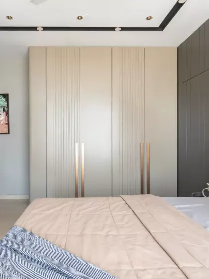 This elegantly curated bedroom exemplifies modern luxury with a seamless blend of muted neutrals and warm earthy tones. The design concept revolves around minimalist sophistication, featuring sleek, floor-to-ceiling wardrobes with subtle metallic accents.