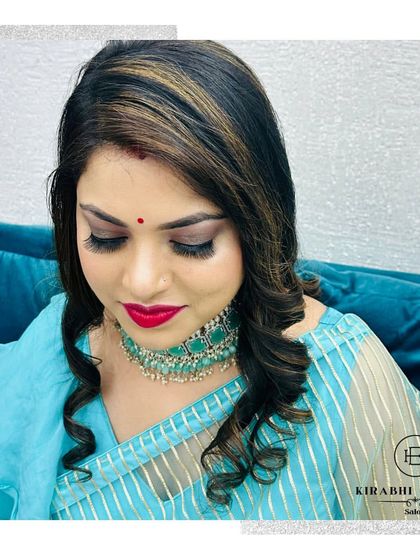 This party makeup look features dramatic winged eyeliner and a bold red lip. The client's hair is styled with soft curls and highlights that frame her face beautifully.
