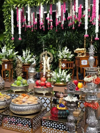A detailed shot of the offerings, including fruits and sweets in silver bowls, set against the garden backdrop.