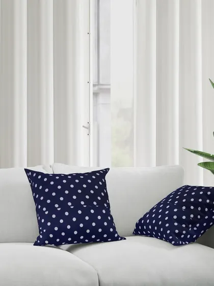 Two navy polka dot cushions placed on a modern white sofa. This demonstrates how the product can be used to add a pop of color and pattern to a living room.