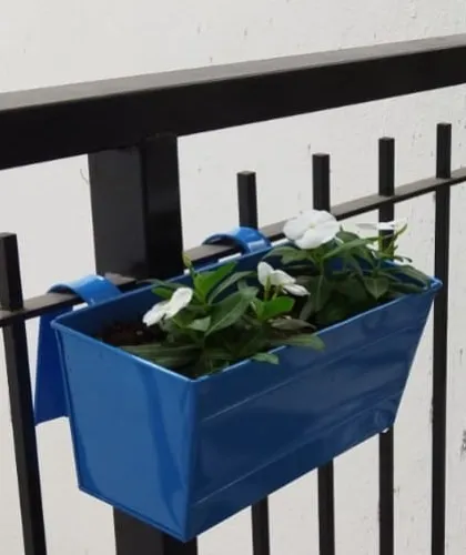 A close up of a blue metal railing planter with white Vinca flowers. These planters are a great way to add color and charm to any balcony railing.