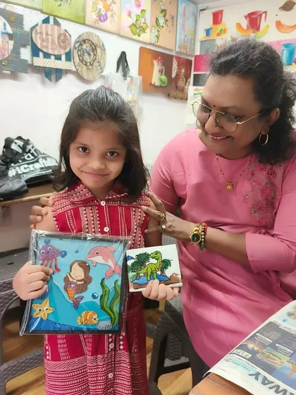 One of our instructors with a young student, proudly showing off the aquarium frame and dinosaur tile she made. We love celebrating every child's unique creations.