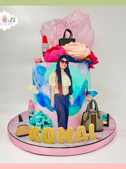 A personalized fashion-themed cake for Komal, featuring her photo alongside edible Gucci bags, makeup, and flowers.