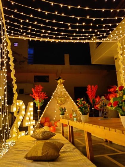 A whimsical terrace setup for a 24th birthday, featuring a teepee tent, illuminated marquee numbers, and a curtain of warm fairy lights.