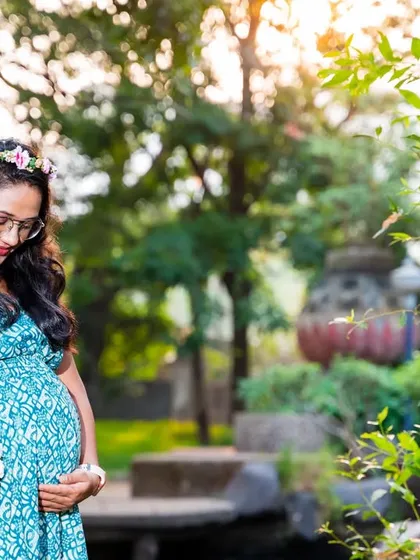 A thoughtful moment in the garden. The mom-to-be, wearing a flower crown, looks down at her bump, holding a basket of fresh flowers.