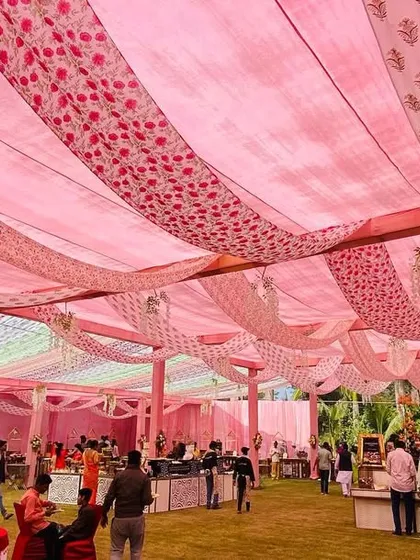 A wide view of a beautiful outdoor tent setup with a ceiling draped in multiple shades and patterns of pink fabric, creating a soft and romantic ambiance.