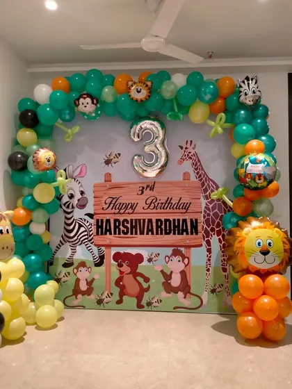 A cute jungle animal theme for a third birthday. The backdrop features a wooden sign design and is framed by a green and orange balloon arch with animal foil balloons.