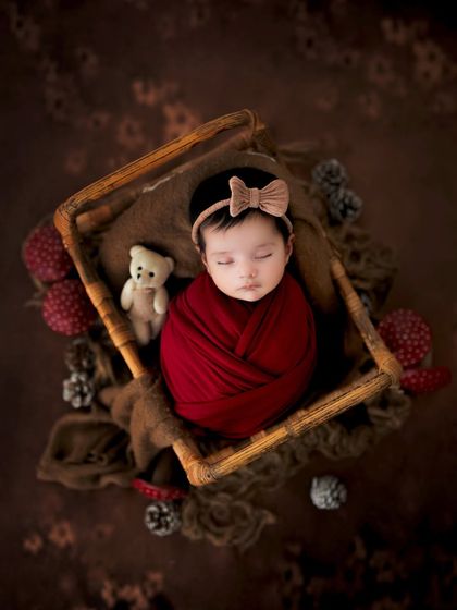 A cozy newborn portrait with warm, earthy tones. The little teddy bear adds a sweet touch to this classic sleeping baby photo.