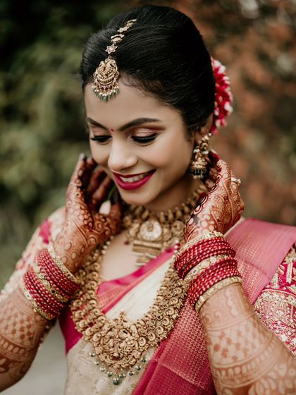 A close-up of a beautiful bride, smiling as she adjusts her traditional gold jewelry.