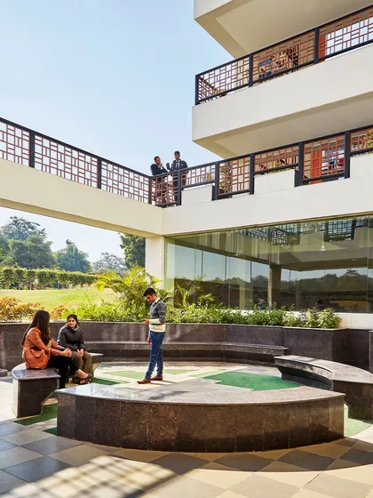 Students gather in a semi-outdoor space at the Sushant School of Design & Architecture. The design encourages interaction and collaboration by providing numerous breakout areas, connecting walkways, and landscaped courts.