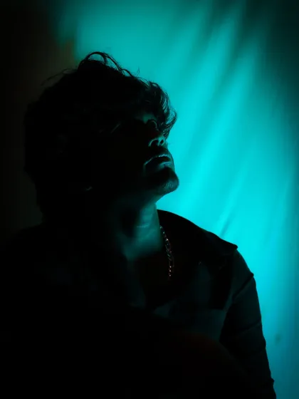 A silhouette portrait using a single teal-colored light source. This technique creates a mysterious and artistic mood by focusing on the subject's profile and the texture of their hair against the light.