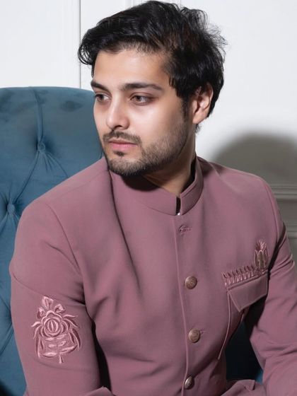 A seated portrait displaying the elegant drape of the pink Prince Coat. The tonal Resham embroidery on the sleeve adds a layer of sophisticated detail without overwhelming the look.
