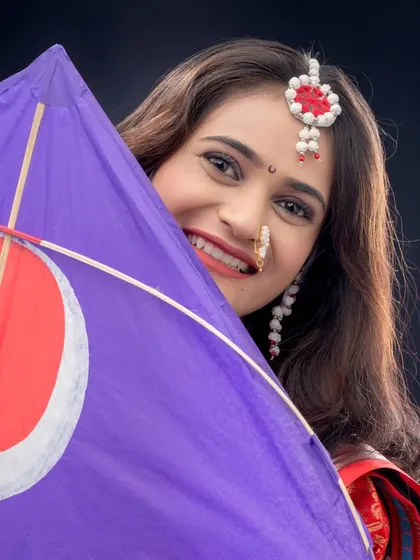 A playful portrait of a woman peeking from behind a kite. Her beautiful smile and traditional halwyache dagine capture the festive spirit of Makar Sankranti.