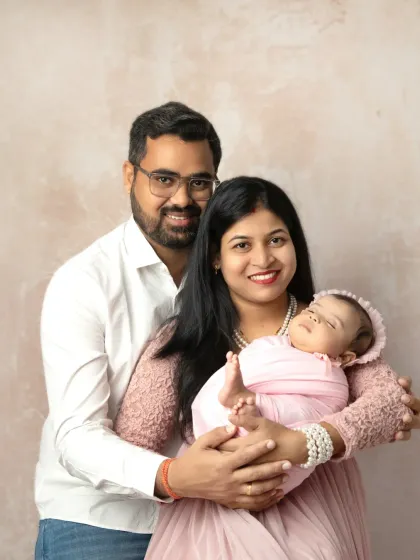 A beautiful first family portrait, with both parents looking lovingly at their newborn baby, who is sleeping peacefully in her mother's arms.