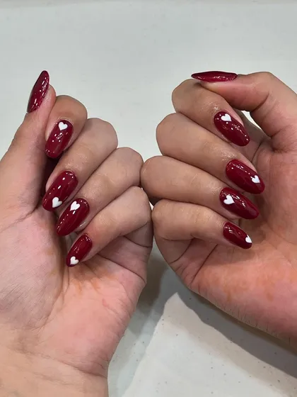 A cute and playful set of red nails with hand-painted white hearts.