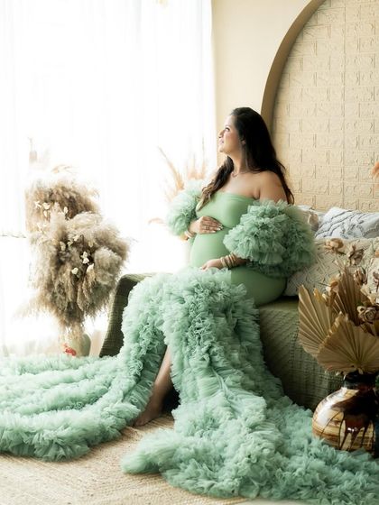 A regal portrait of a mother-to-be in a stunning mint green gown, seated on our boho studio bed.