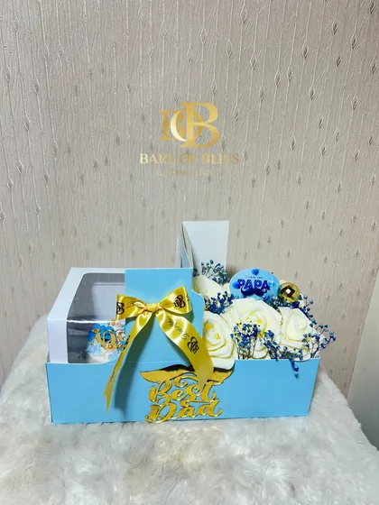 A blue-themed Father's Day hamper containing a bento cake and a box of white and blue roses, accented with a "Best Dad" sign.