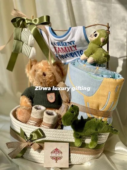 A different angle of the 'Current Family Favorite' hamper, showing the thoughtful arrangement of the teddy bear, dinosaur toys, and baby booties in a sturdy rope basket.