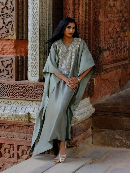The flowing elegance of the sage green kaftan is captured as the model poses, highlighting its asymmetrical hem and graceful drape.
