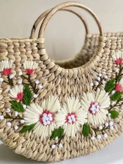A close-up of a handwoven bag featuring delicate white and pink floral embroidery. This design showcases the fine, detailed craftsmanship that goes into each of our unique, artisan-made accessories.