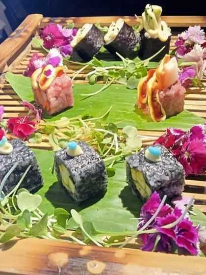 An example of our artistic sushi plating. Here, a variety of sushi rolls are garnished with edible flowers and microgreens on a bamboo platter, showcasing our attention to detail and presentation.