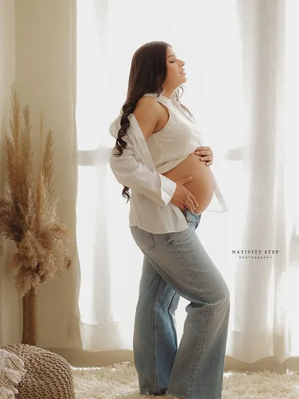 A serene and beautiful portrait by the window. The natural light and casual attire create a timeless and authentic image of motherhood.