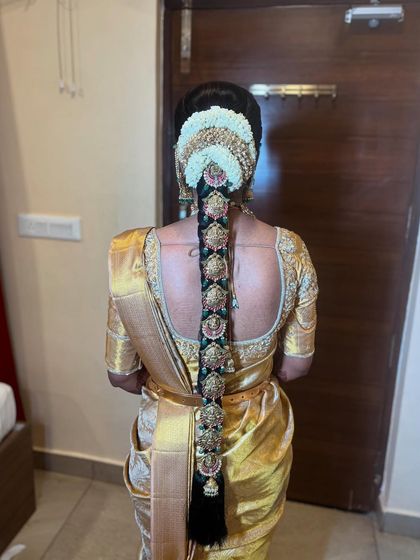 An intricate bridal braid featuring multiple 'Jada Billa' clips with green and pink stone accents, perfectly complementing the bride's golden saree.