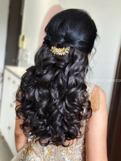 An elegant half-up style with a twisted crown and bouncy curls, adorned with a beautiful gold leaf accessory.