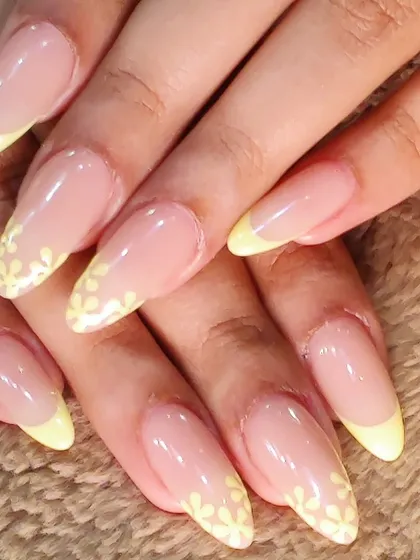 A fresh take on a classic. These elegant, long almond nails feature a delicate pastel yellow French tip, with one nail on each hand adorned with a beautiful, hand-painted white floral design.