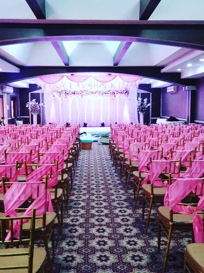 No event is too large. We can transform expansive halls into beautiful ceremonial spaces, ensuring every guest has a great view. This setup includes coordinated seating with pink sashes and a fully decorated stage.