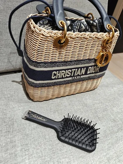 A personalized GHD hairbrush for 'Aarshia', pictured next to a classic Christian Dior bag. It shows how a personalized touch can make an everyday item feel just as luxurious as a high fashion accessory.