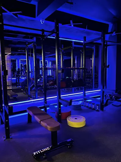 Our strength section is equipped for serious gains. This shot highlights one of our two squat racks and weight plates, all set against our signature blue ambient lighting that creates an energetic workout environment.
