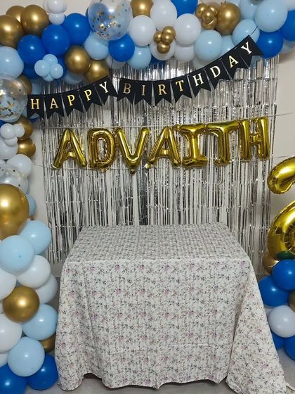 Even a simple corner can be transformed for a celebration. This home setup for a 2nd birthday features an L-shaped balloon garland, a shimmer curtain, and foil balloons for the name and age.
