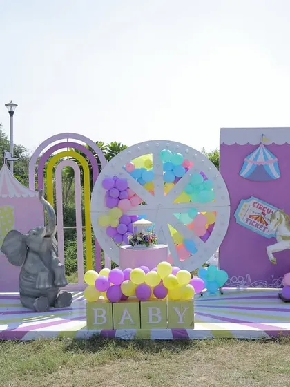An outdoor pastel carnival wonderland created for a twins' birthday celebration. This wide shot displays the full themed stage with a Ferris wheel, carousel horses, and hot air balloon props, all coordinated in a soft, dreamy color palette perfect for a sunny day.