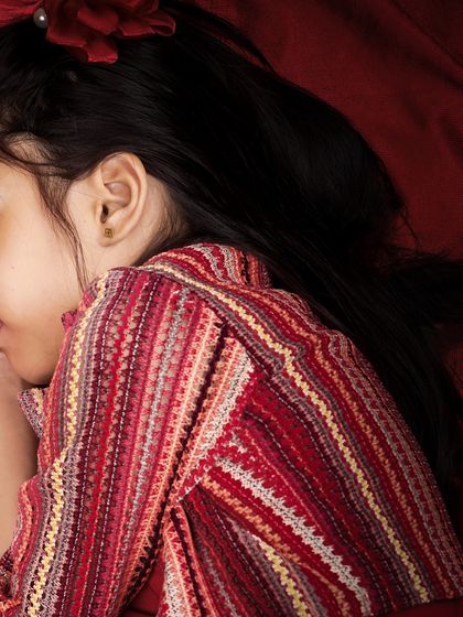 A quiet, candid moment of a young girl resting on a rich, red fabric. The simplicity of the shot creates a beautiful and thoughtful portrait.